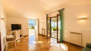 A room with a TV, a small table, a bench, a radiator, and a sliding glass door leading to a patio. - AMORE RENTALS - Villa Raffaella with Private Pool and Sea View (Sant´Agata sui Due Golfi)