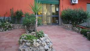 A courtyard with a stone wall, a palm tree, and a building with an air conditioning unit. - b&b Borgo Pileri (Mazzarino)