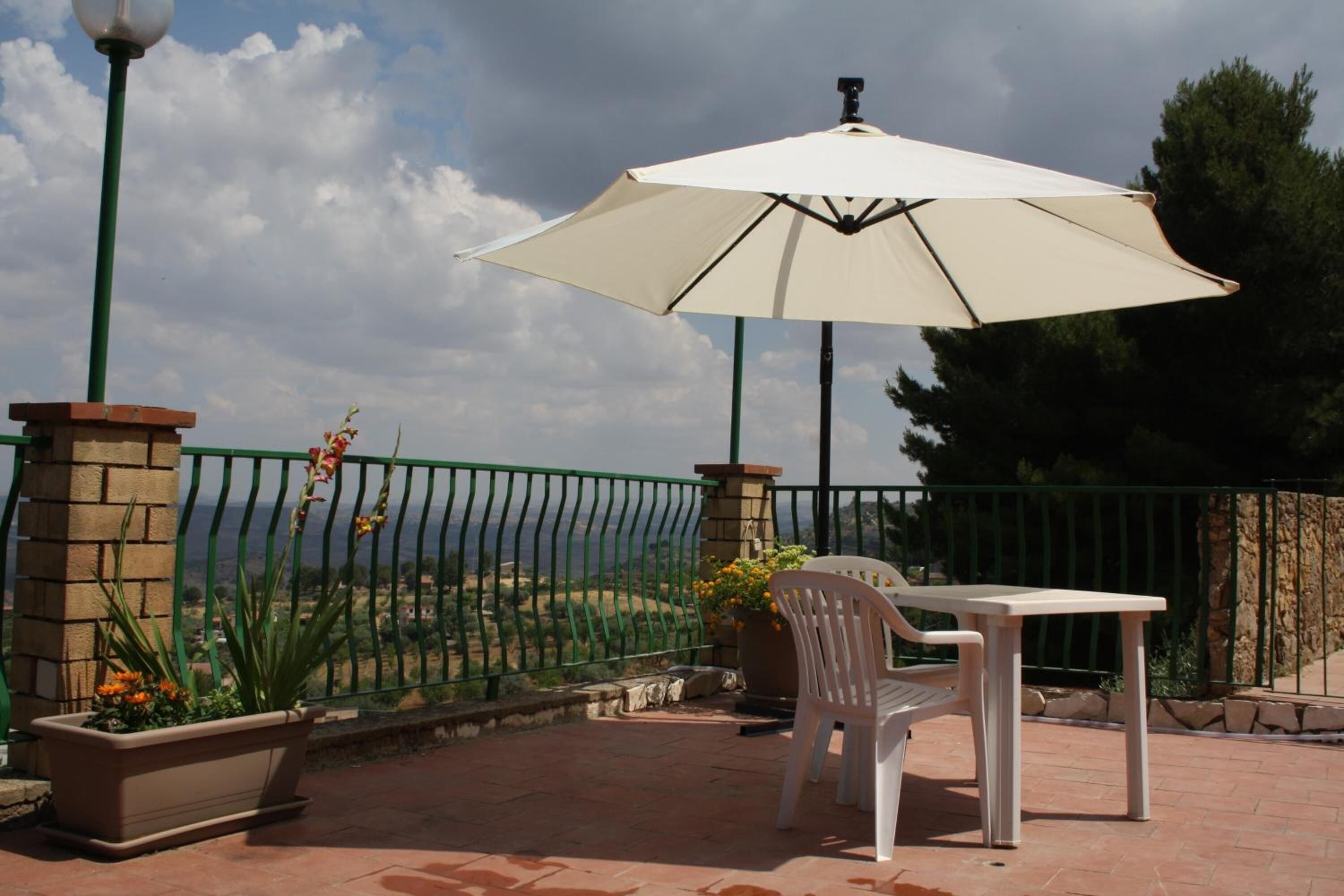 An outdoor patio with a table and chairs, a white umbrella, and a view of the sea.