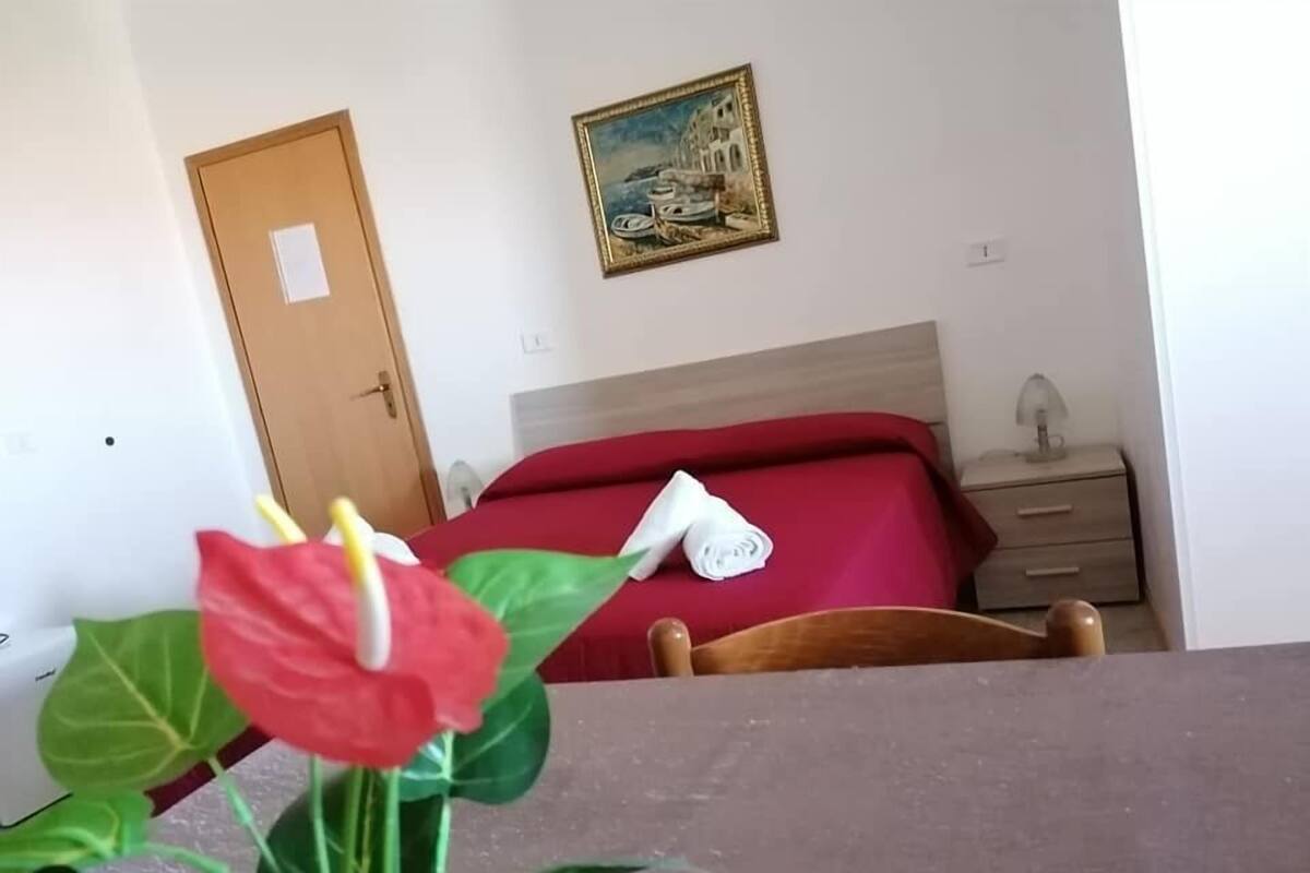 A hotel room with a bed, a nightstand, a painting, and a potted plant.