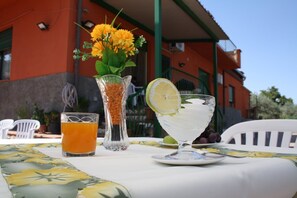 A table with a glass of orange juice, a pitcher of lentils, and a glass of white beverage with a lemon slice, set outdoors with a building in the background. - b&b Borgo Pileri (Mazzarino)
