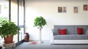 A living room with a grey sofa, red and grey cushions, a potted plant, and a vase on the floor. - b&b Borgo Pileri (Mazzarino)
