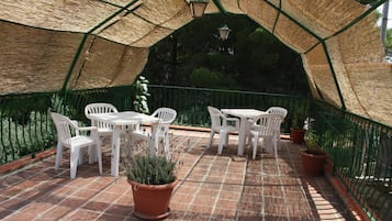 An outdoor patio with white plastic chairs and tables, surrounded by a green metal fence and potted plants.