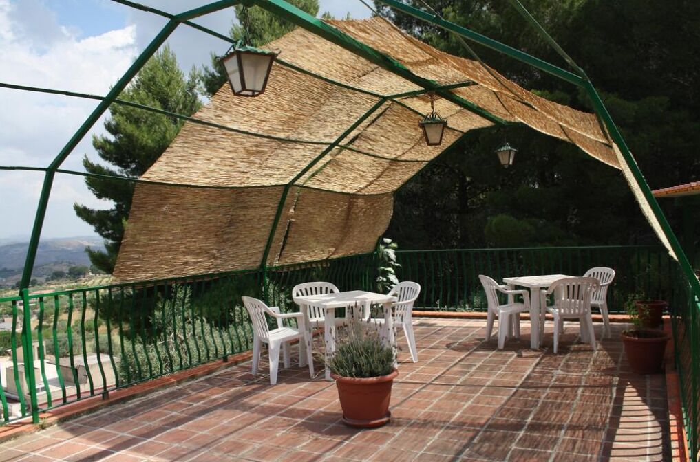 Veranda coperta con tavolo e sedie, una pianta in vaso e vista sul paesaggio circostante.