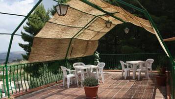 Veranda coperta con tavolo e sedie, una pianta in vaso e vista sul paesaggio circostante.