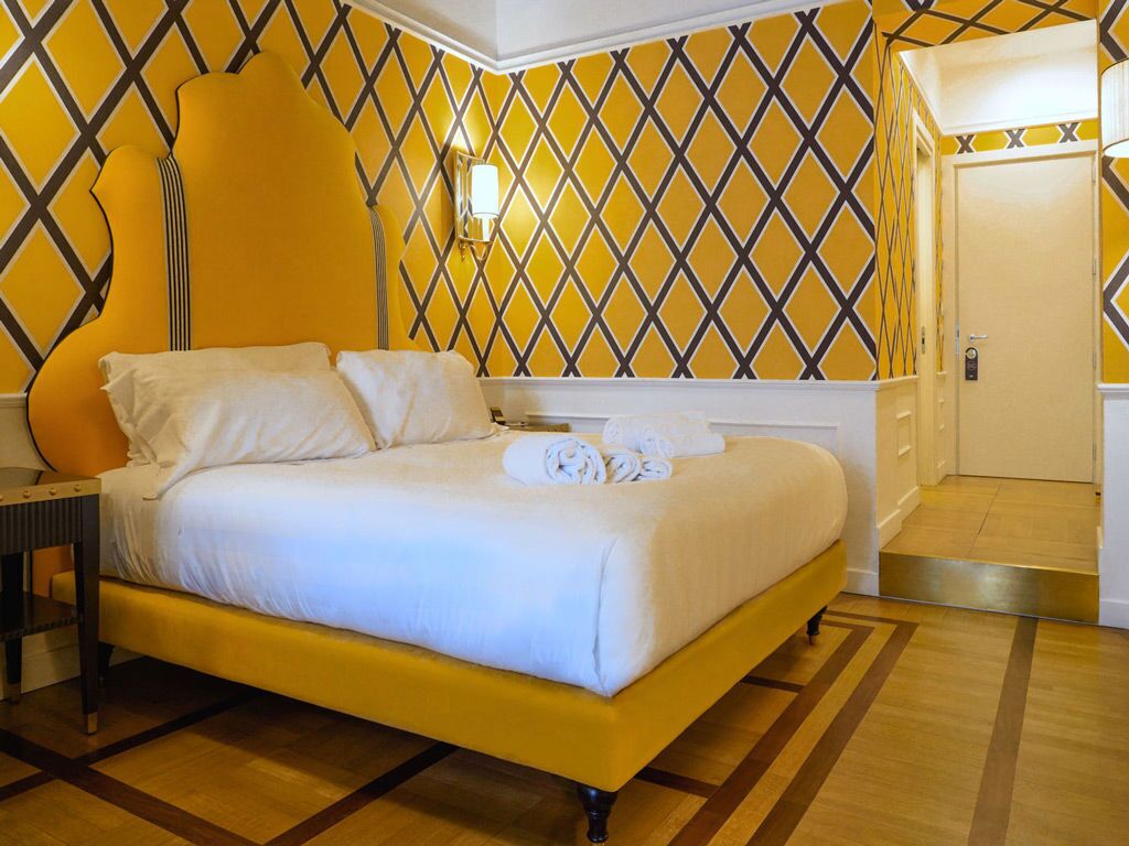 A hotel room with a bed, a nightstand, a wall-mounted lamp, and a door.