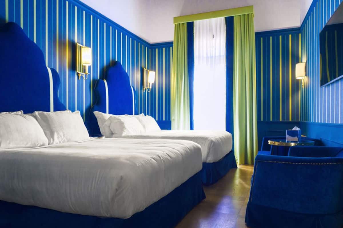 A hotel room with two beds, a desk, and a mirror.