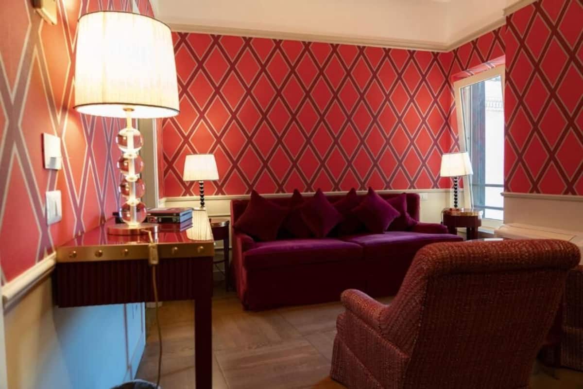 A room with a red patterned wallpaper, a purple sofa, and two lamps.
