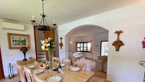 Et spiseområde med et træbord dækket til seks personer, omgivet af stole. Der er en lysekrone over bordet, og en vase med blomster står på bordet.