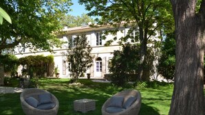 A building with a large garden, two wicker chairs, and a tree.