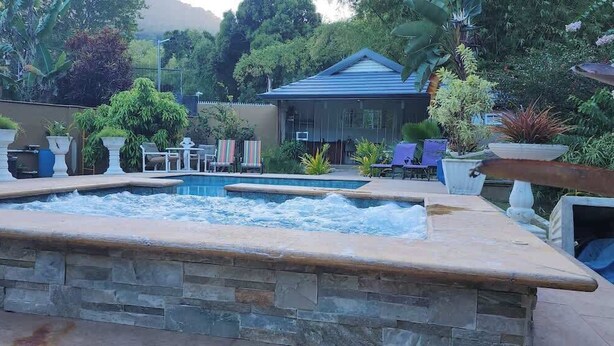 Une piscine bordée de pierres, entourée de plantes en pot et de mobilier d’extérieur.