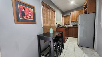 A kitchen with a dining table, wooden cabinets, a refrigerator, and a window with blinds.