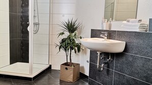 Ein modernes Badezimmer mit einer Duschkabine aus Glas, einem Waschbecken mit Spiegel und einer Topfpflanze.