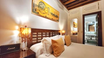 Een hotelkamer met een bed, nachtkastje, lamp, schilderij en een spiegel in de badkamer.