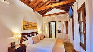 A bedroom with a wooden ceiling, a bed with white linens, a painting on the wall, and a TV mounted on the wall. - Entre Dos Aguas Hotel Boutique (Toledo)