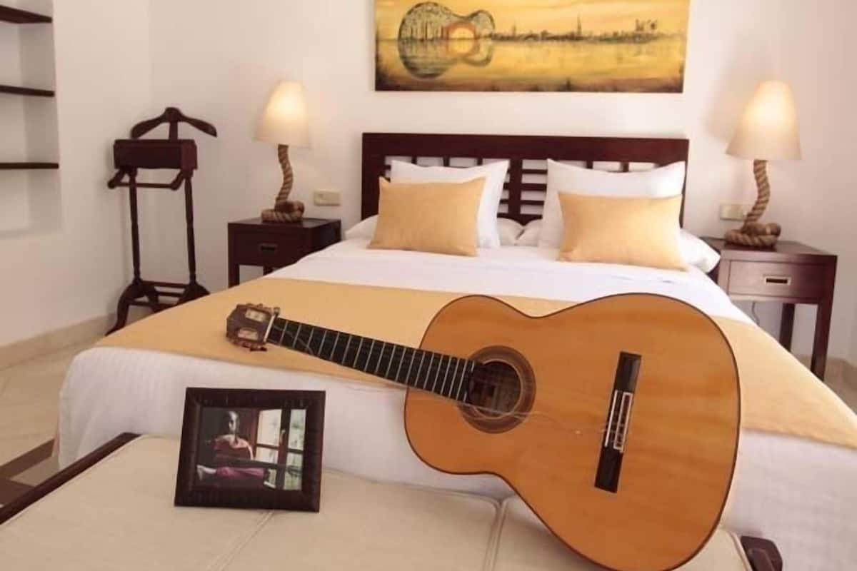 A bedroom with a bed, a guitar, a picture frame, and a painting on the wall.