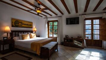 A bedroom with a bed, bedside lamps, a ceiling fan, a TV, and a window with curtains.