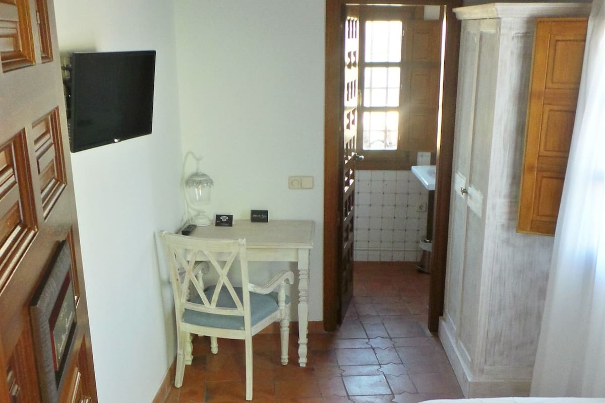A bedroom with a bed, a desk, and a chair. There is a television mounted on the wall.