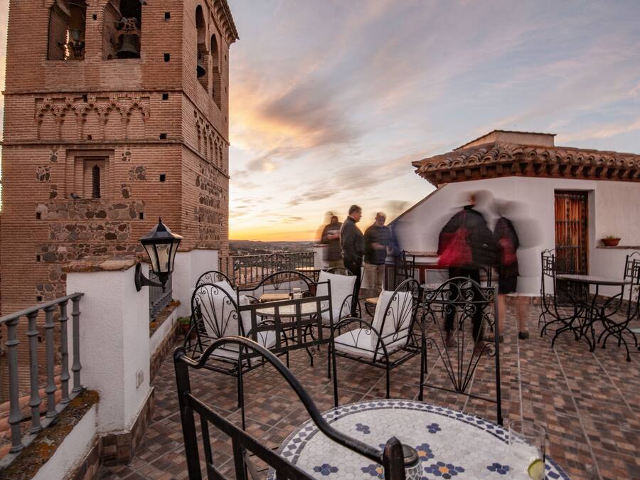 A terrace with outdoor seating, a bell tower, and a view of the sunset.