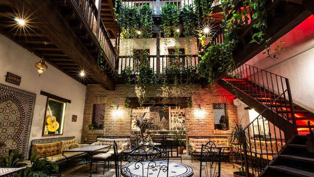 A cozy courtyard with a round table, sofas, and chairs, surrounded by potted plants and a staircase. - Entre Dos Aguas Hotel Boutique (Toledo)