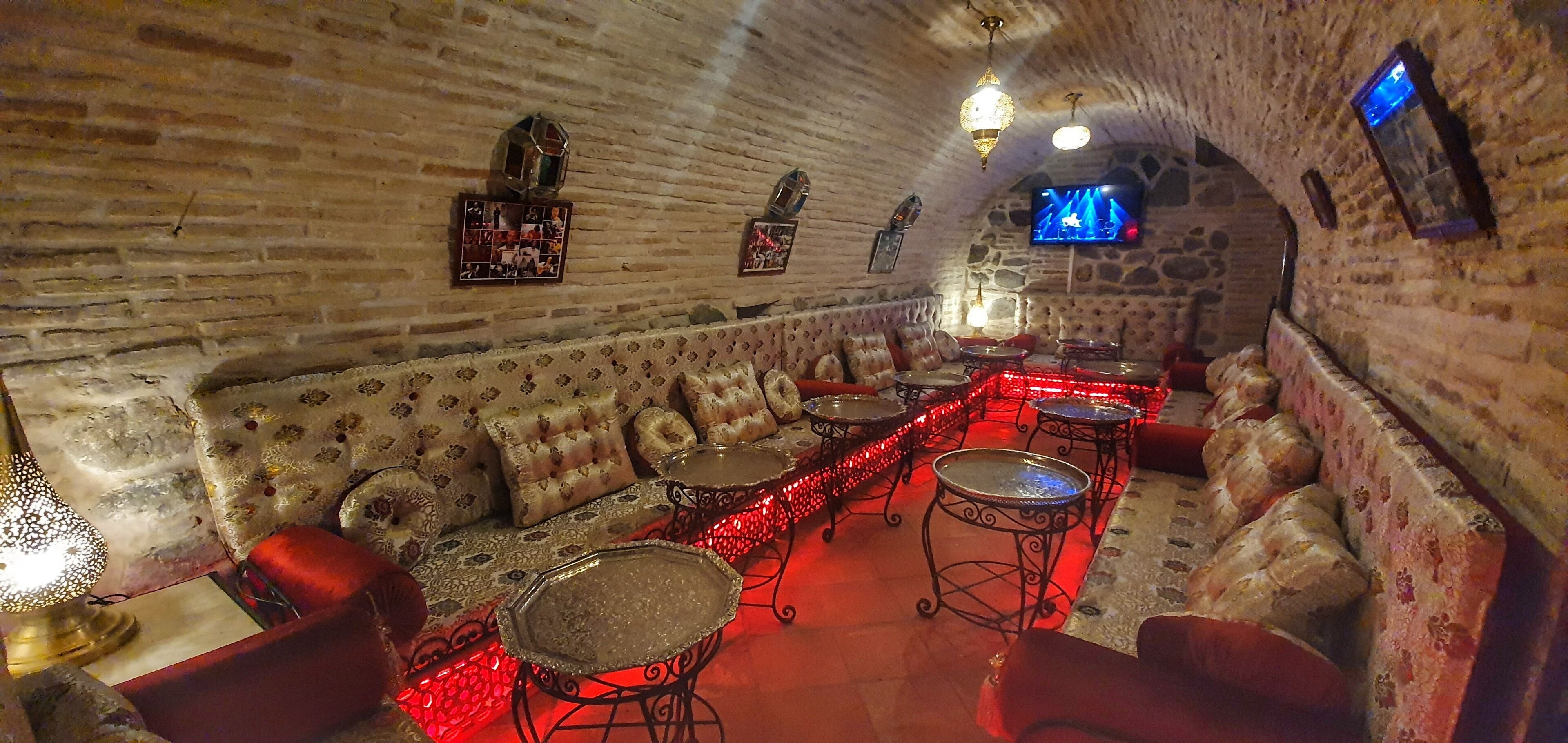 Une pièce chaleureuse et faiblement éclairée, avec des murs en pierre, un long canapé et plusieurs petites tables.