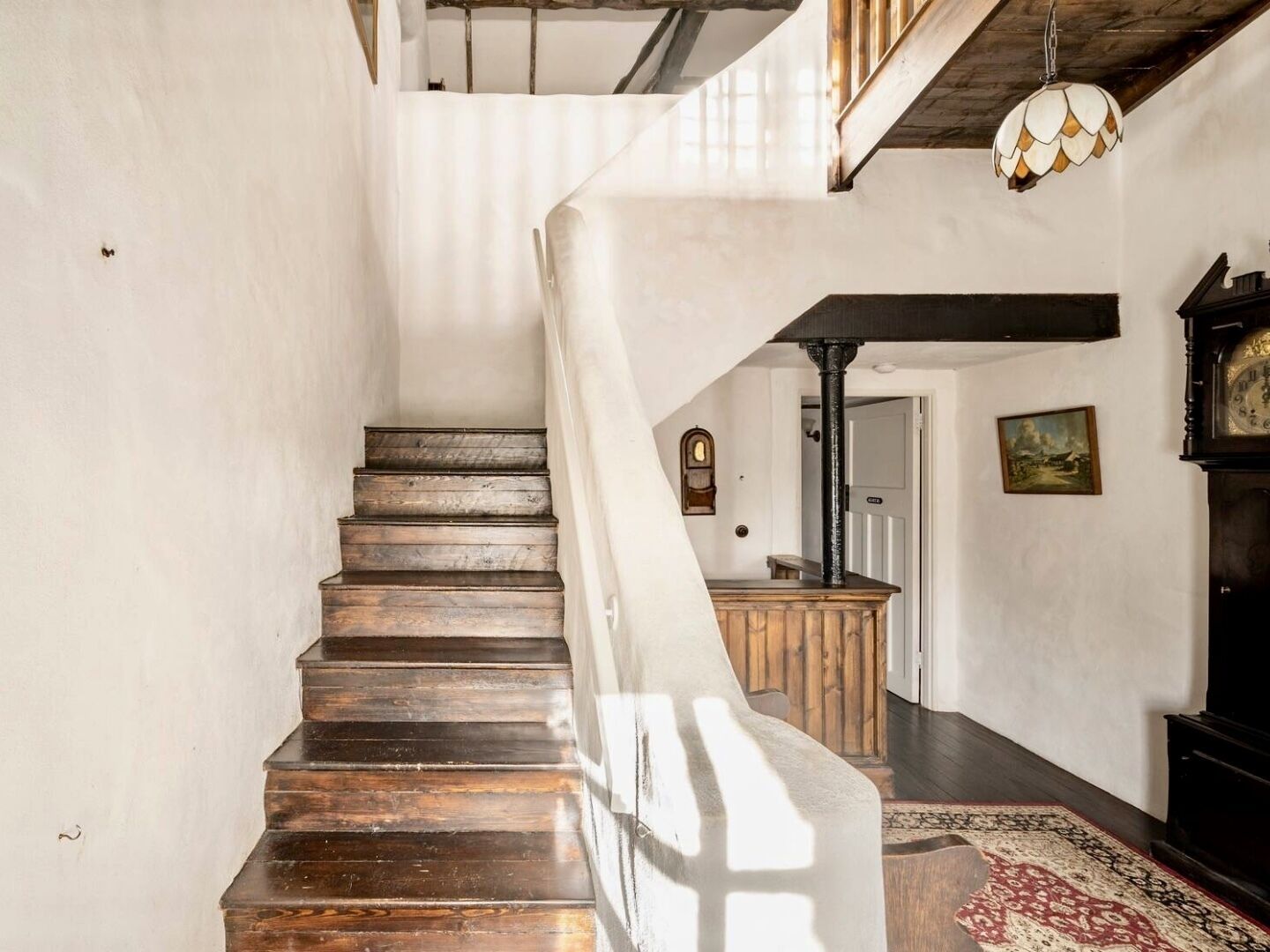 A staircase with wooden steps leading to a landing area with a wooden bench and a black clock.