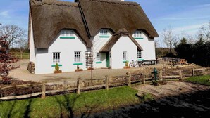 Une maison traditionnelle à toit de chaume, aux murs blancs et aux encadrements de fenêtres verts.