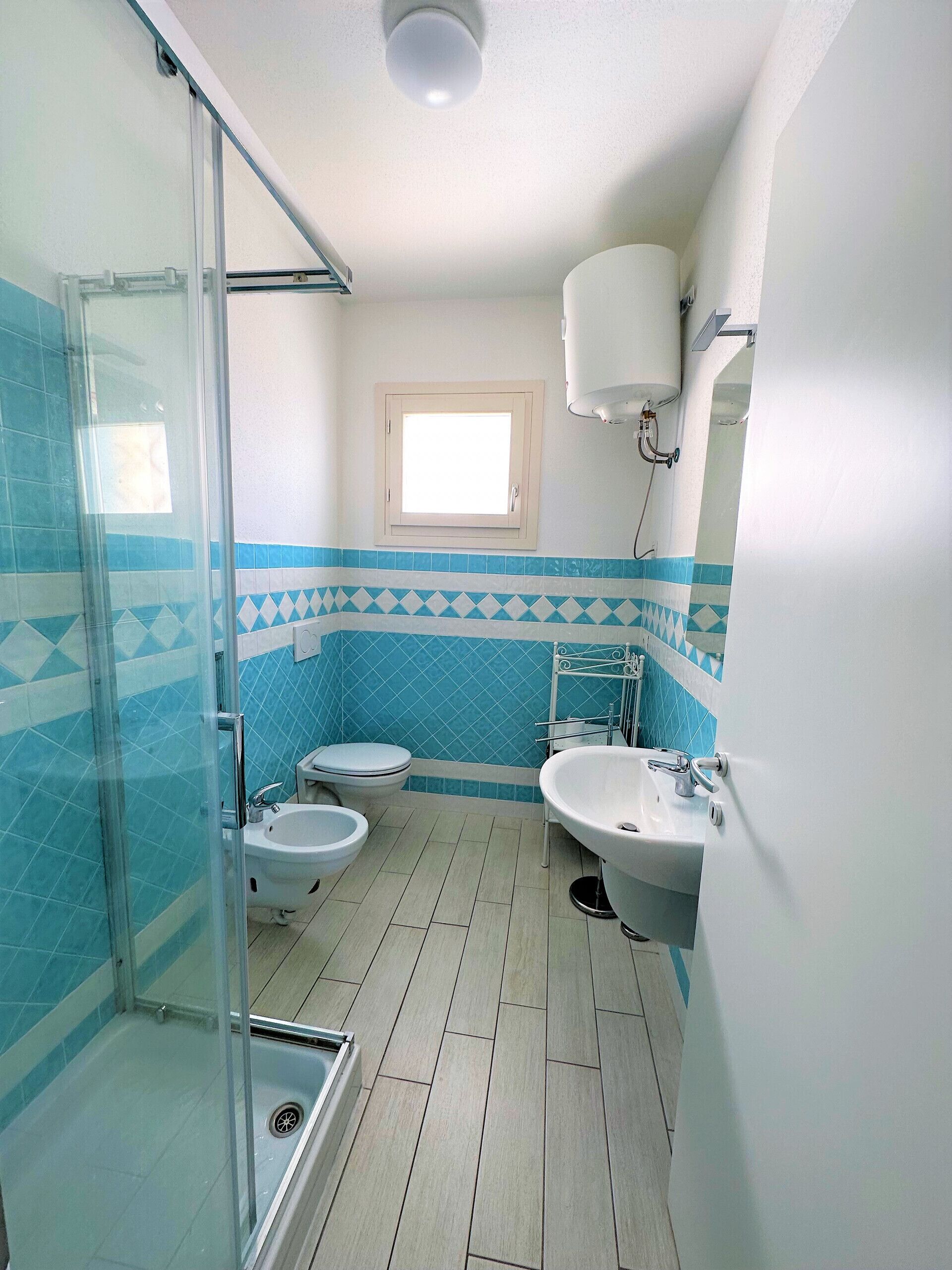 A bathroom with a glass shower enclosure, a toilet, a bidet, a sink, and a window.