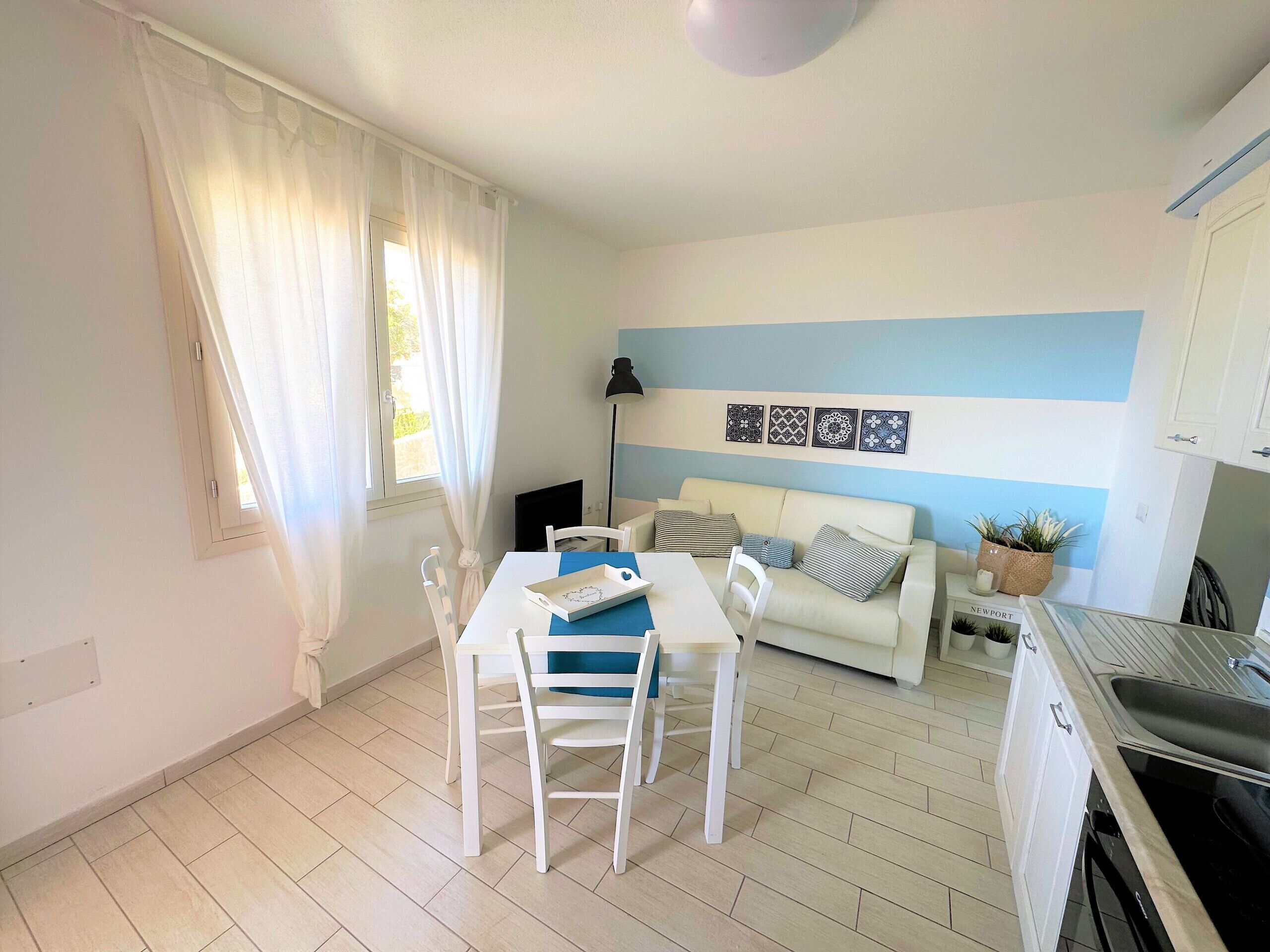 Um espaço compacto para viver, com área de refeições, sofá, cozinha e janela com cortinas.