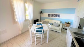Ett kompakt bostadsutrymme med en matplats, en soffa, ett kök och ett fönster med gardiner.