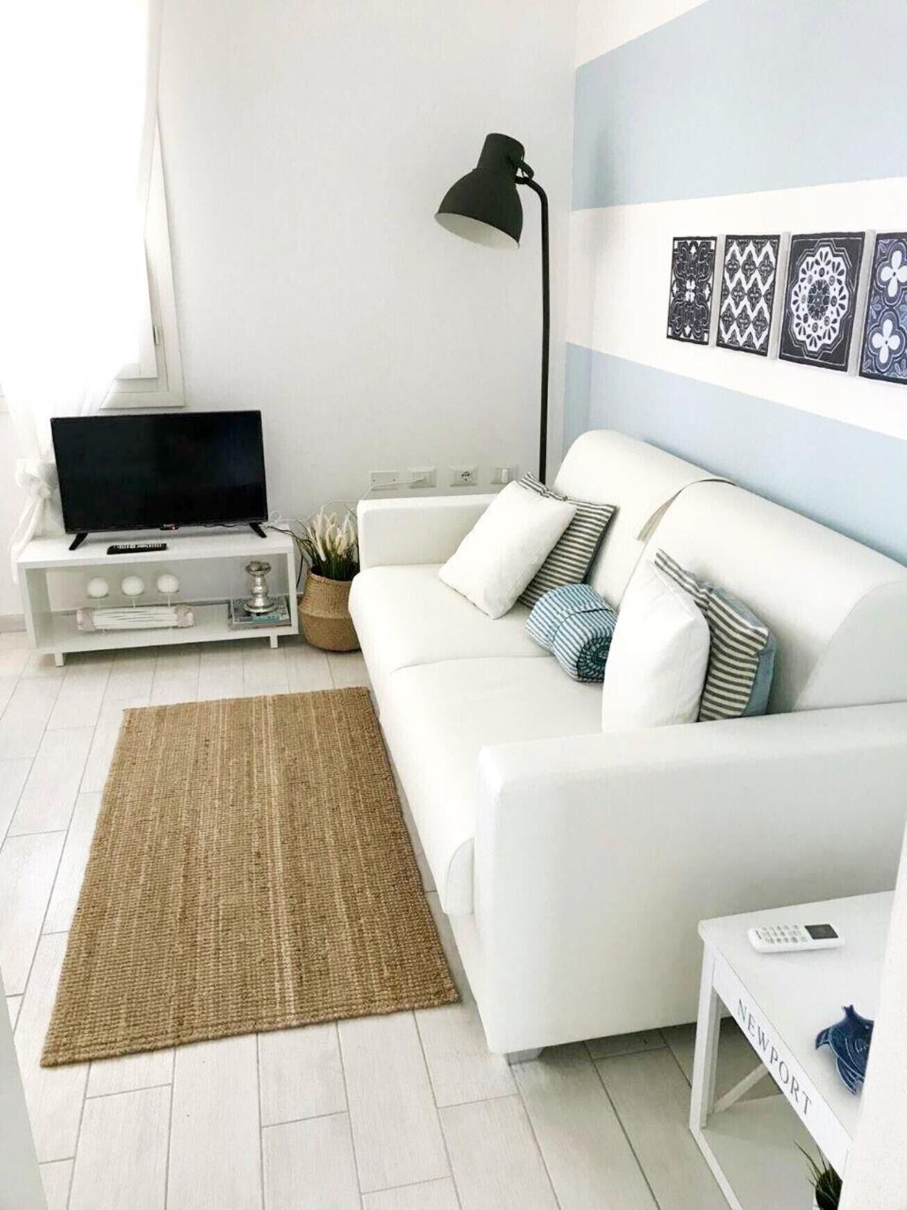A modern living room with a white sofa, a flat-screen TV, a lamp, and decorative wall art.