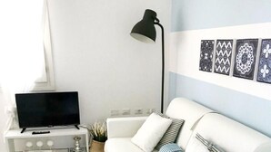 Ett modernt vardagsrum med en vit soffa, en platt-TV, en lampa och dekorativ väggkonst.