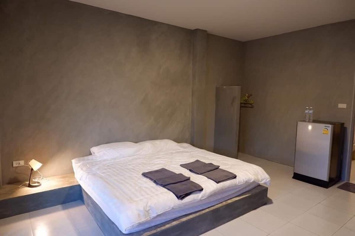 Una habitación de hotel moderna con una cama grande, una mesita de noche con lámpara y un refrigerador.