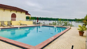 A swimming pool with a tiled edge, lounge chairs, and a building with a red roof in the background. - Water View Villa-monthly rate discount (EVERGLADES CITY)