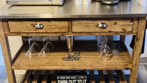A kitchen counter with a microwave, coffee maker, and two mugs. Below, there is a wooden shelf with wine glasses and a decorative sign. - Water View Villa-monthly rate discount (EVERGLADES CITY)
