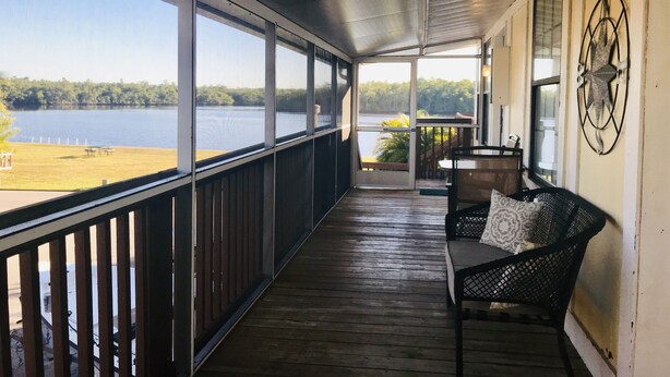 A covered porch with a view of a lake, a wooden deck, a bench, and a table with chairs. - Water View Villa-monthly rate discount (EVERGLADES CITY)
