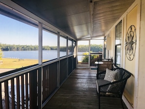 A covered porch with a view of a lake, a wooden deck, a bench, and a table with chairs.
