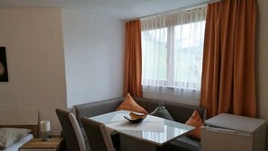 A compact hotel room with a small dining table, a sofa, a single bed, and a compact kitchenette.