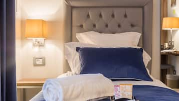 Una cama bien hecha con una toalla blanca y una bandeja con una tarjeta y un bolígrafo, un cabecero y dos lámparas fijadas a la pared.