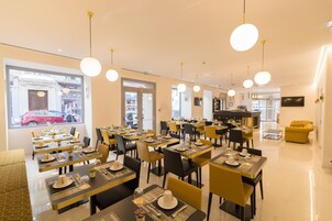 Un comedor moderno con varias mesas y sillas, una zona de bar y grandes ventanales con vistas a la calle.