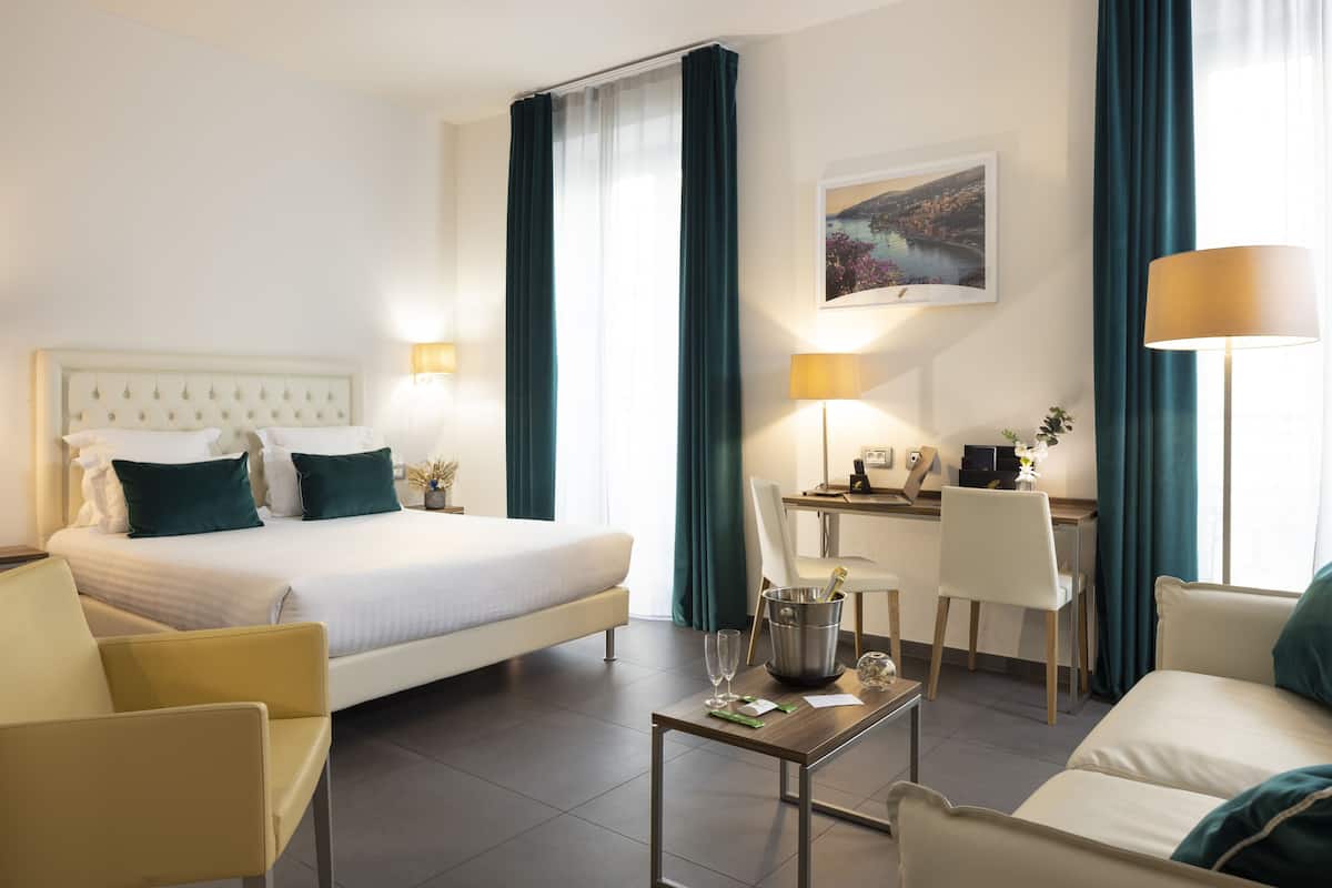 A hotel room with a bed, a desk, a chair, a coffee table, and a couch.