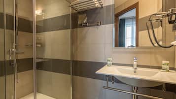 A modern bathroom with a glass shower enclosure, a white sink with a mirror above, and a towel rack.