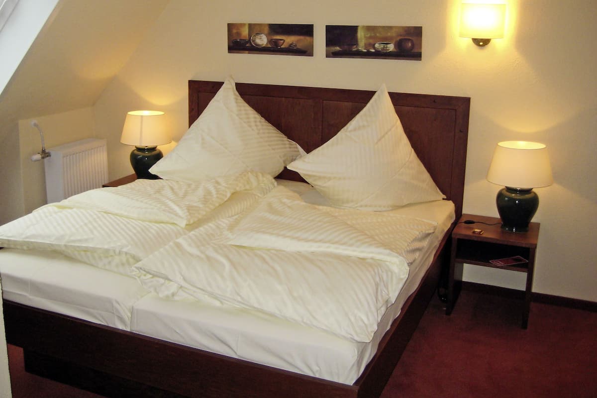 A neatly made bed with a wooden headboard, two bedside lamps, and a radiator on the wall.