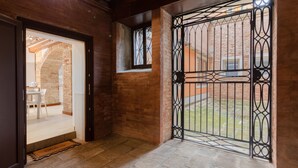 A hallway with a brick wall, a metal gate, and a door leading to a room with a white table and chairs. - Loft on two levels exposed beam (Venezia)