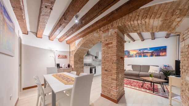 A modern living room with a dining area, featuring exposed brick walls, wooden beams, and a cozy seating arrangement. - Loft on two levels exposed beam (Venezia)