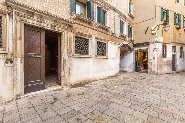 A historic building with a large wooden door, a brick-paved courtyard, and a shop with a green awning.