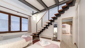 A bedroom with two beds, a staircase, and a view of the city through large windows. - Loft on two levels exposed beam (Venezia)