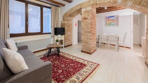 A living room with a sofa, a red patterned rug, a TV, and a dining area with a table and chairs. - Loft on two levels exposed beam (Venezia)