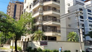 A multi-story building with balconies, a signboard, and a palm tree in the foreground. - Suites Natalia Enseada (Guarujá)