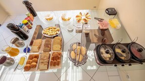 A breakfast buffet with various pastries, breads, and beverages. - Suites Natalia Enseada (Guarujá)